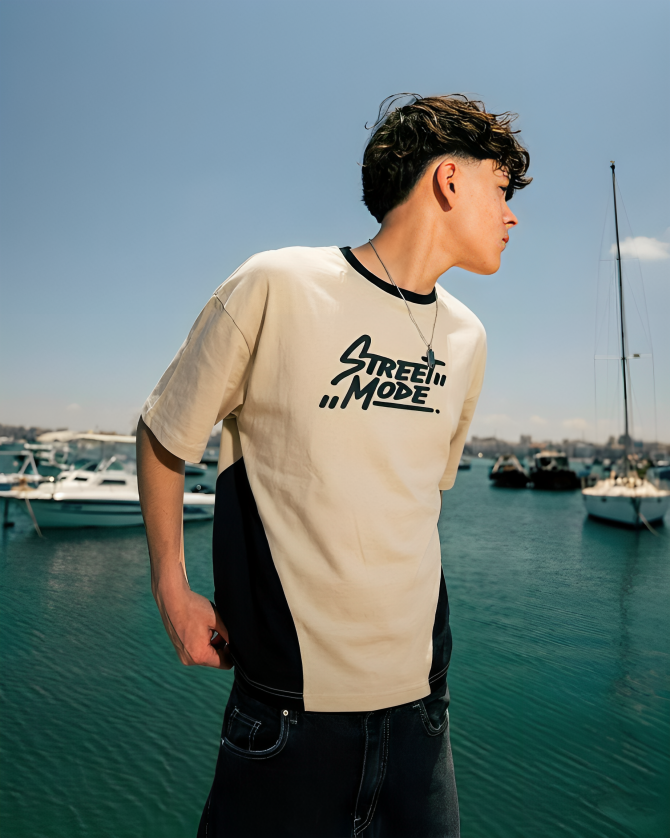 Person wearing a 'Street Mode' t-shirt by a marina with boats and clear blue sky.