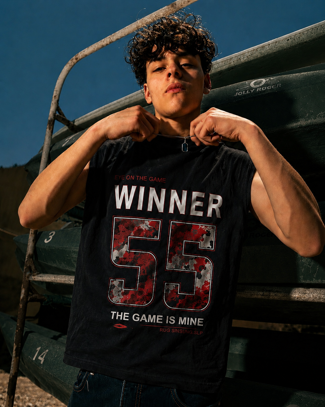 A young man wearing a black graphic tank top with 'WINNER 55' printed on the front, posing outdoors in front of a green boat under a clear blue sky.
