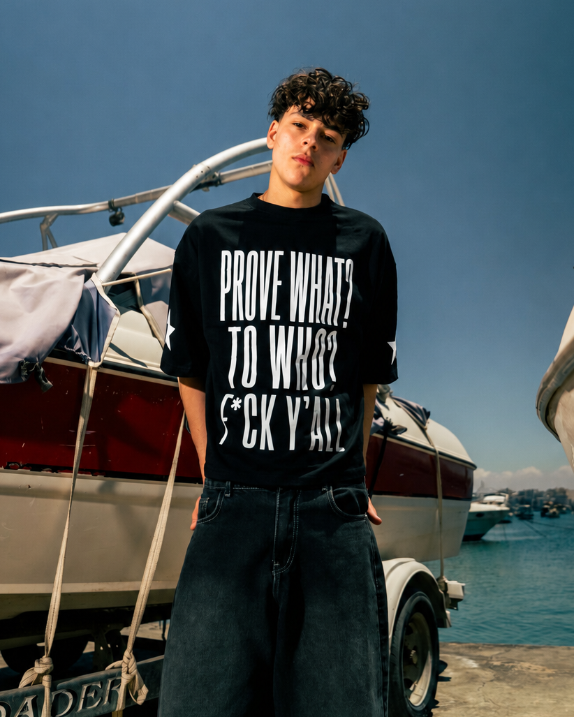 Person wearing a black t-shirt with text standing near boats on a dock.