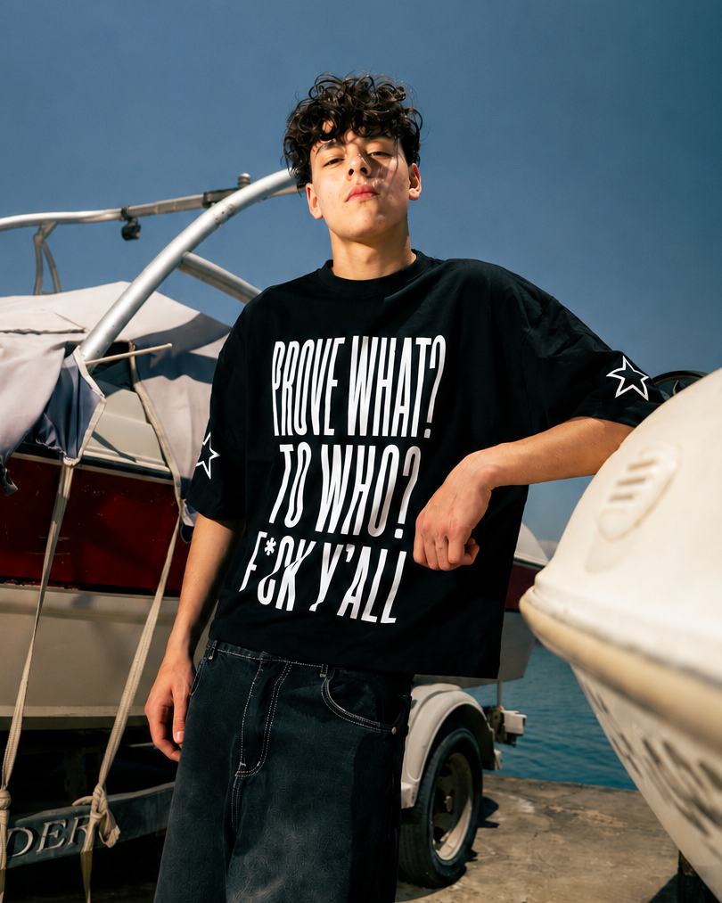 Person wearing a black t-shirt with text standing near boats on a dock.