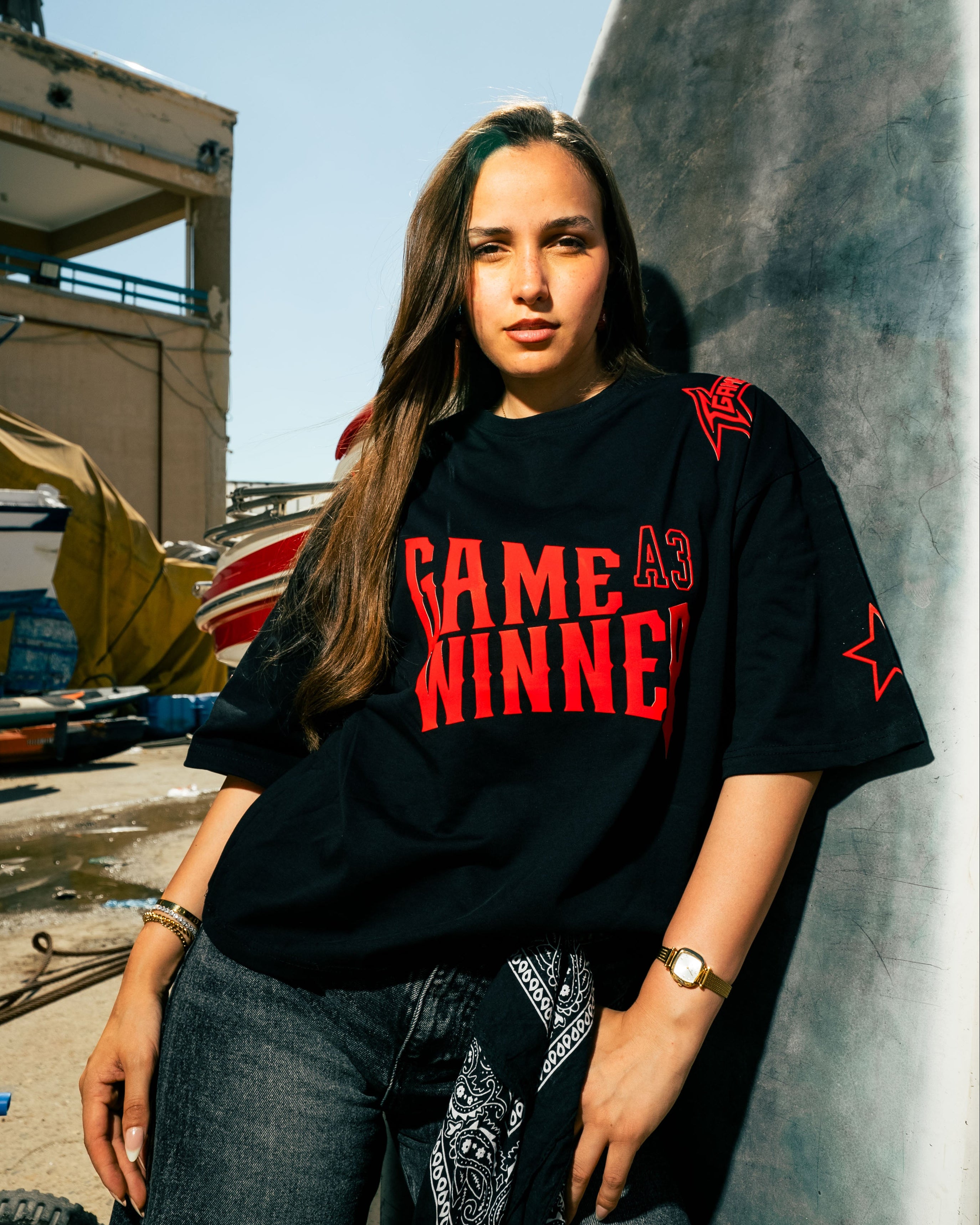 Person wearing a black t-shirt with red text, standing outdoors near a concrete wall.