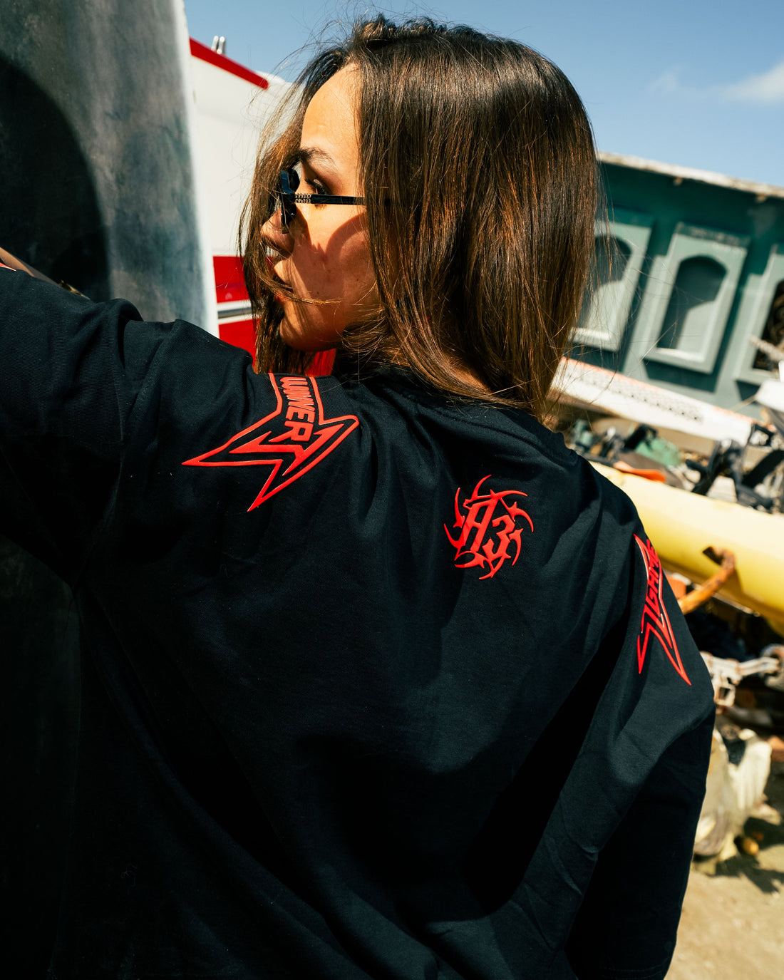 Person wearing a black t-shirt with red text, standing outdoors near a concrete wall.