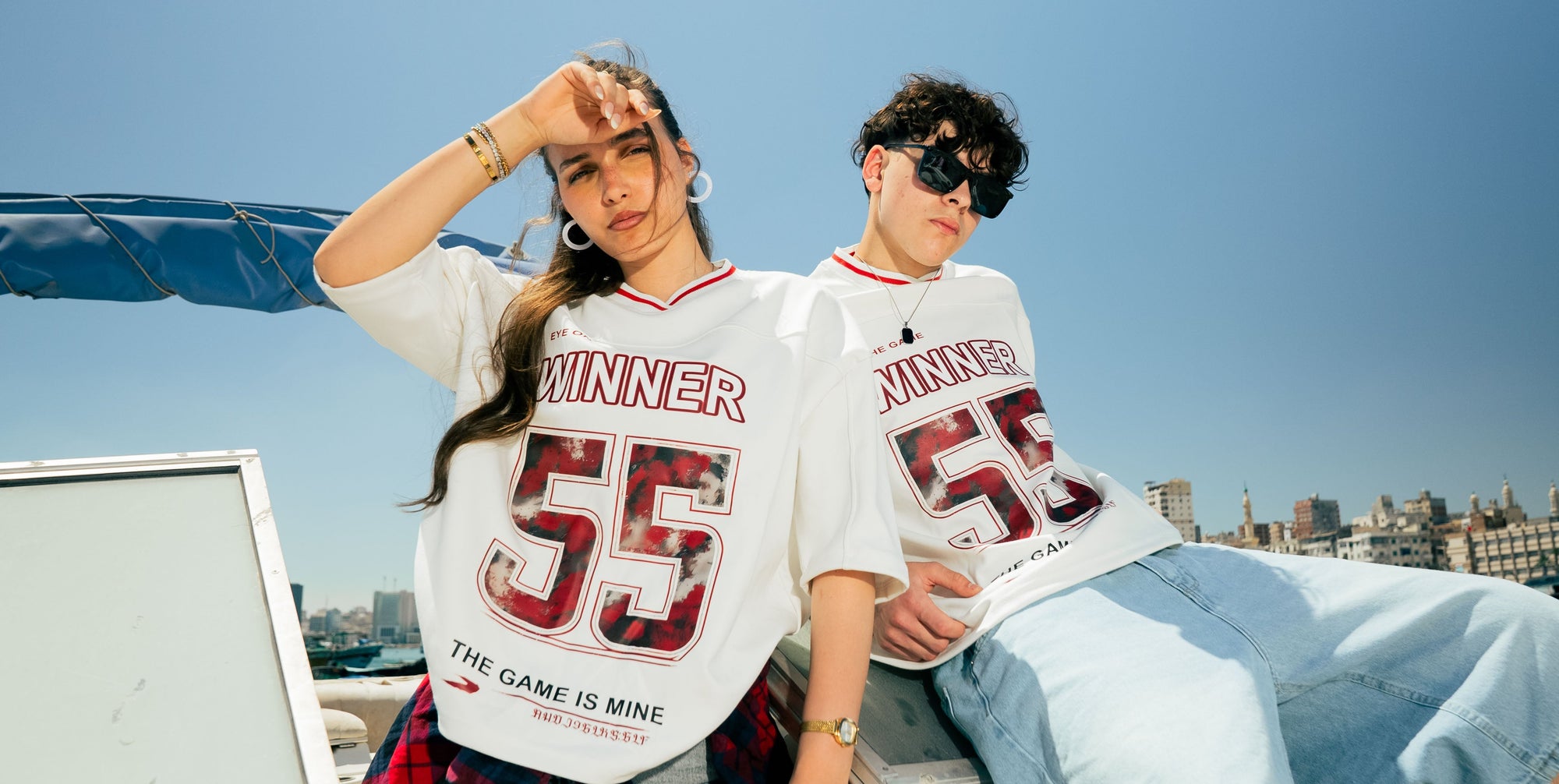 Two people wearing 'Winner' jerseys with the number 55 against a city skyline.