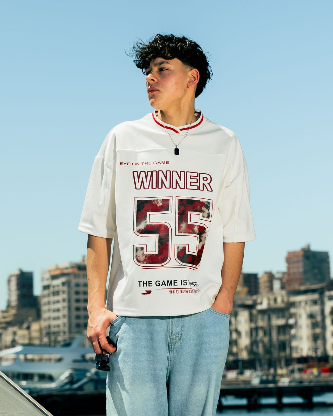 Person wearing a white t-shirt with red text standing on a boat with a cityscape in the background