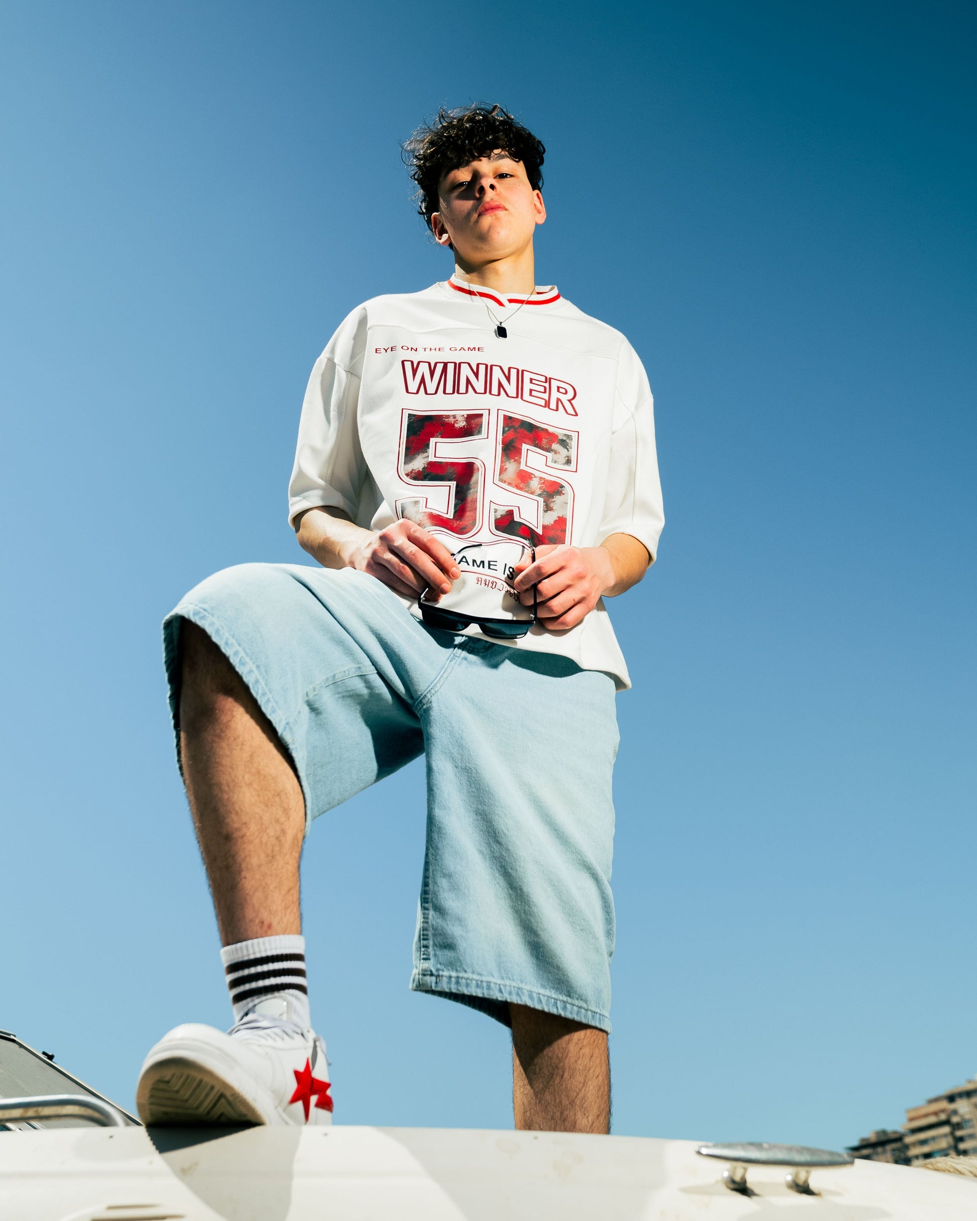 Person wearing a 'Winner' t-shirt and light blue shorts against a clear blue sky.