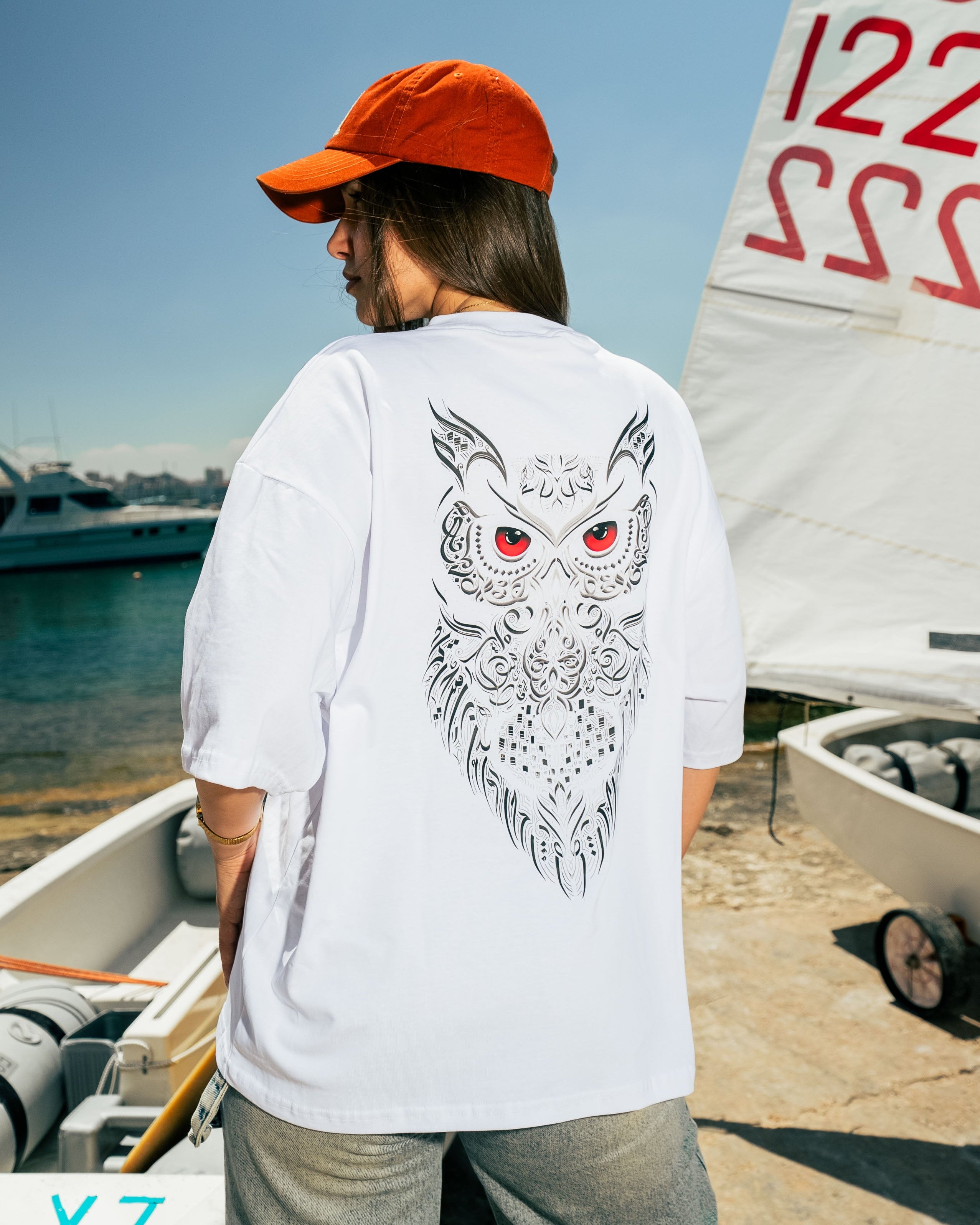 Person wearing a white t-shirt with an owl design by a boat on a dock.
