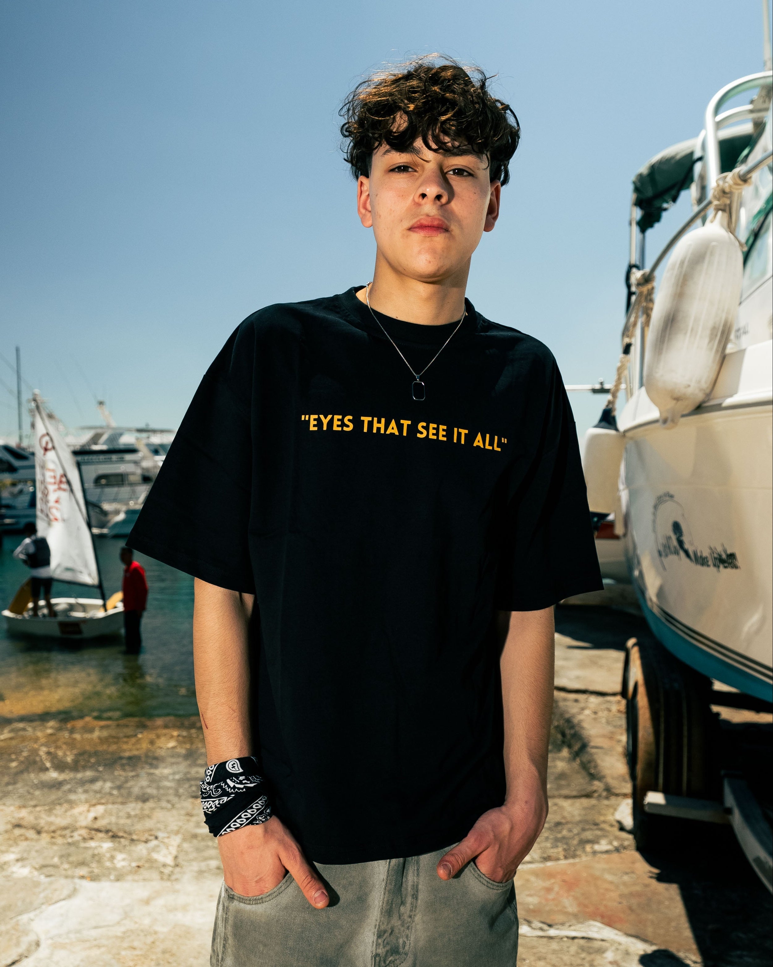Person wearing a black t-shirt with text standing on a dock with boats in the background