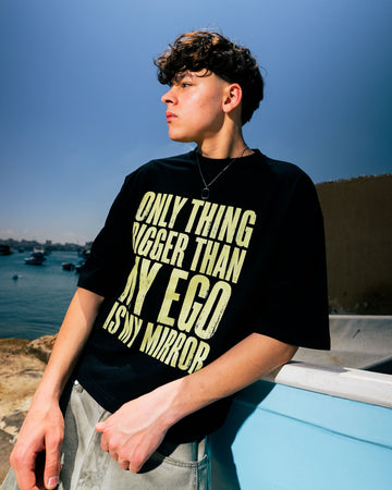 Person wearing a black t-shirt with yellow text by a body of water.