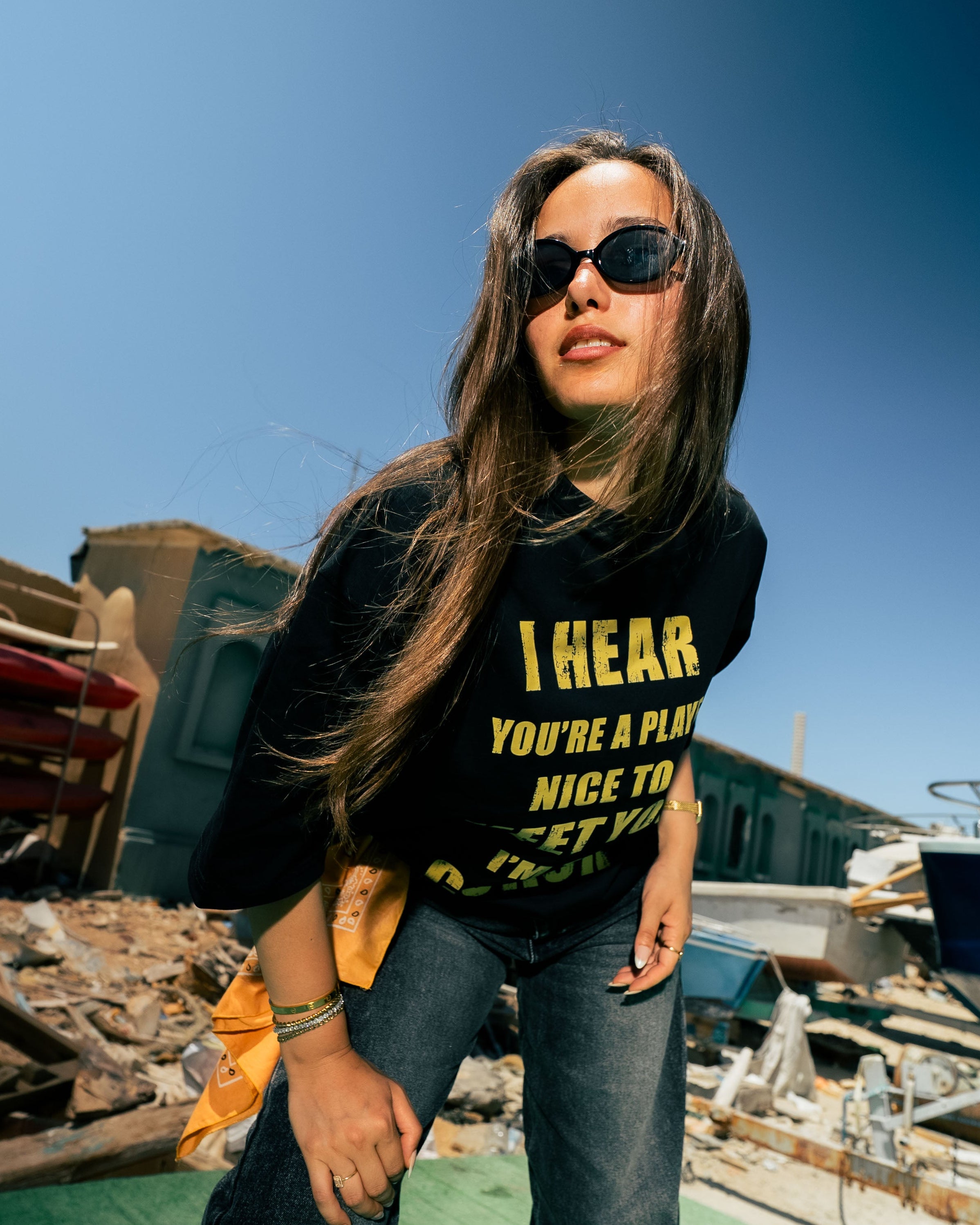 Woman wearing a black t-shirt with yellow text, standing against a blue sky.