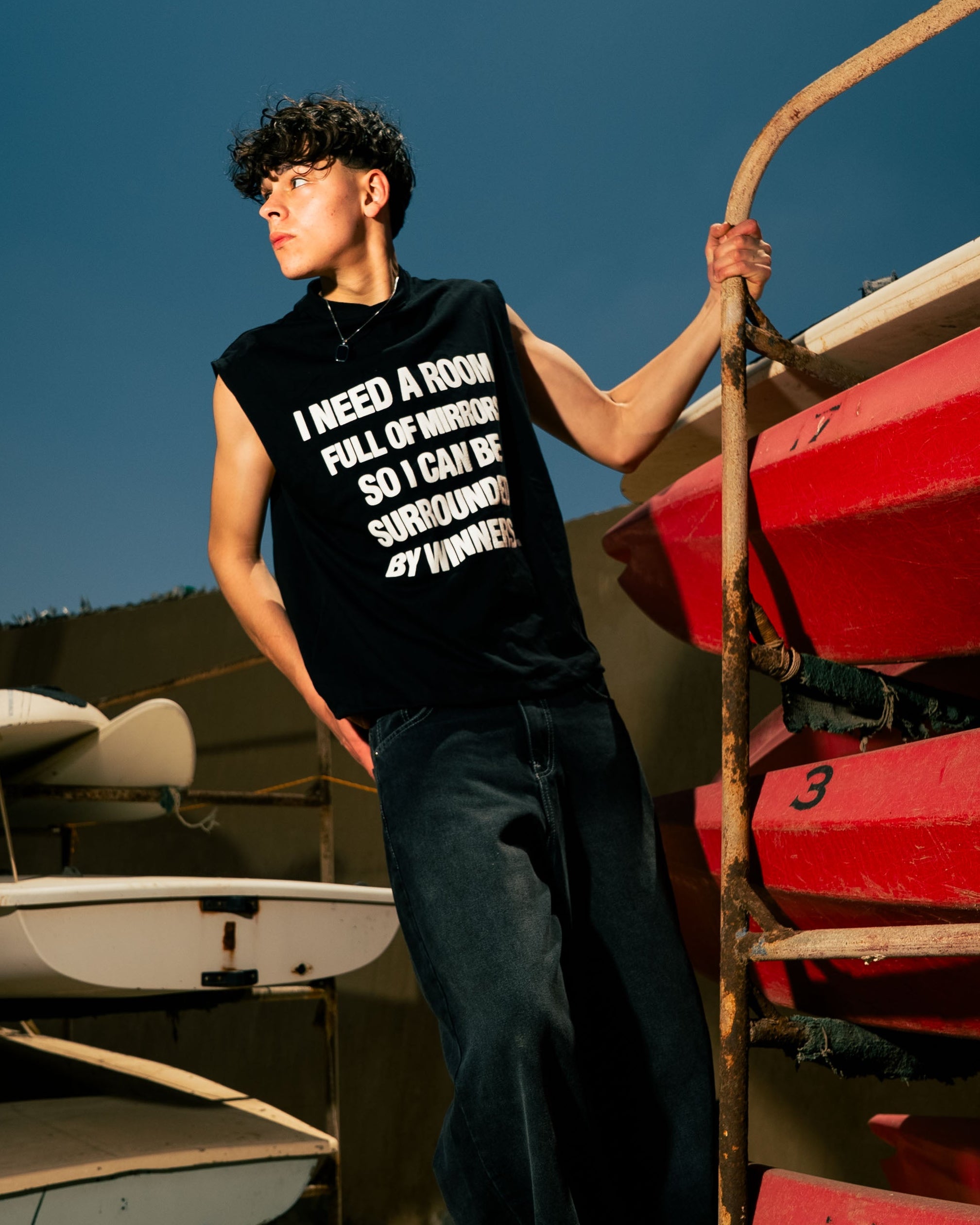 Person wearing a black t-shirt with text, standing next to red kayaks on a dock.