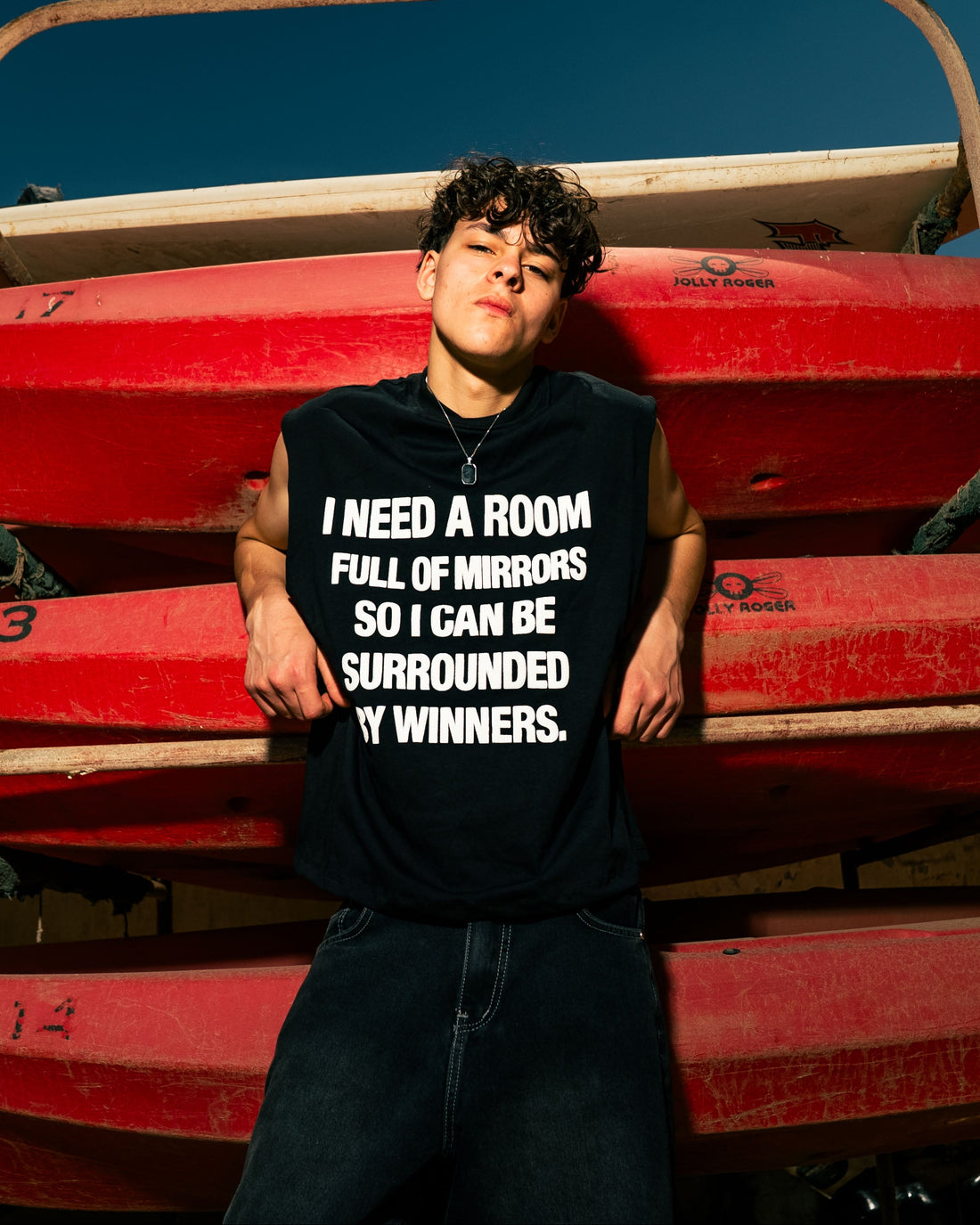 Person wearing a black t-shirt with text standing in front of red kayaks.