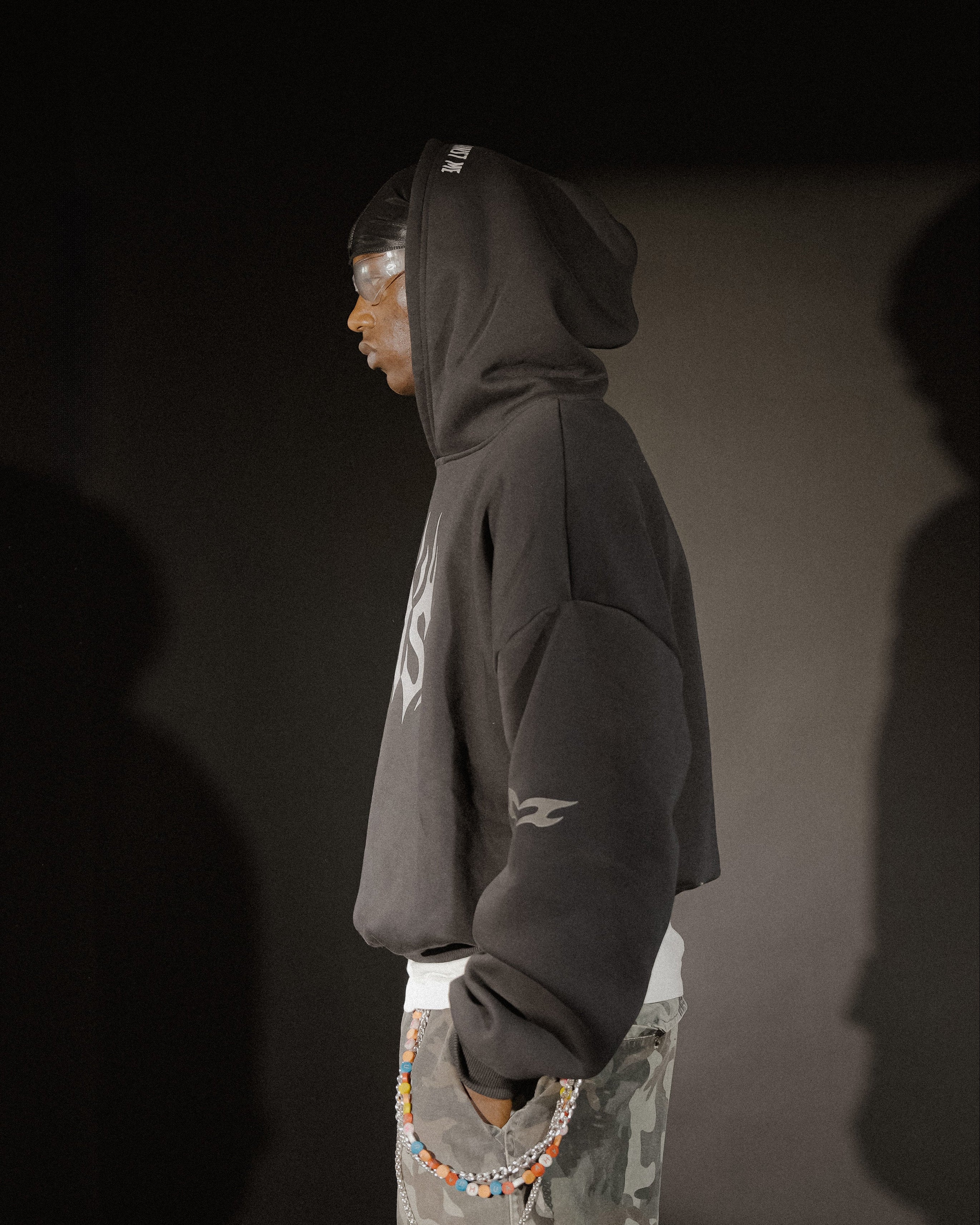 Person wearing a dark hoodie and camouflage pants against a dark background
