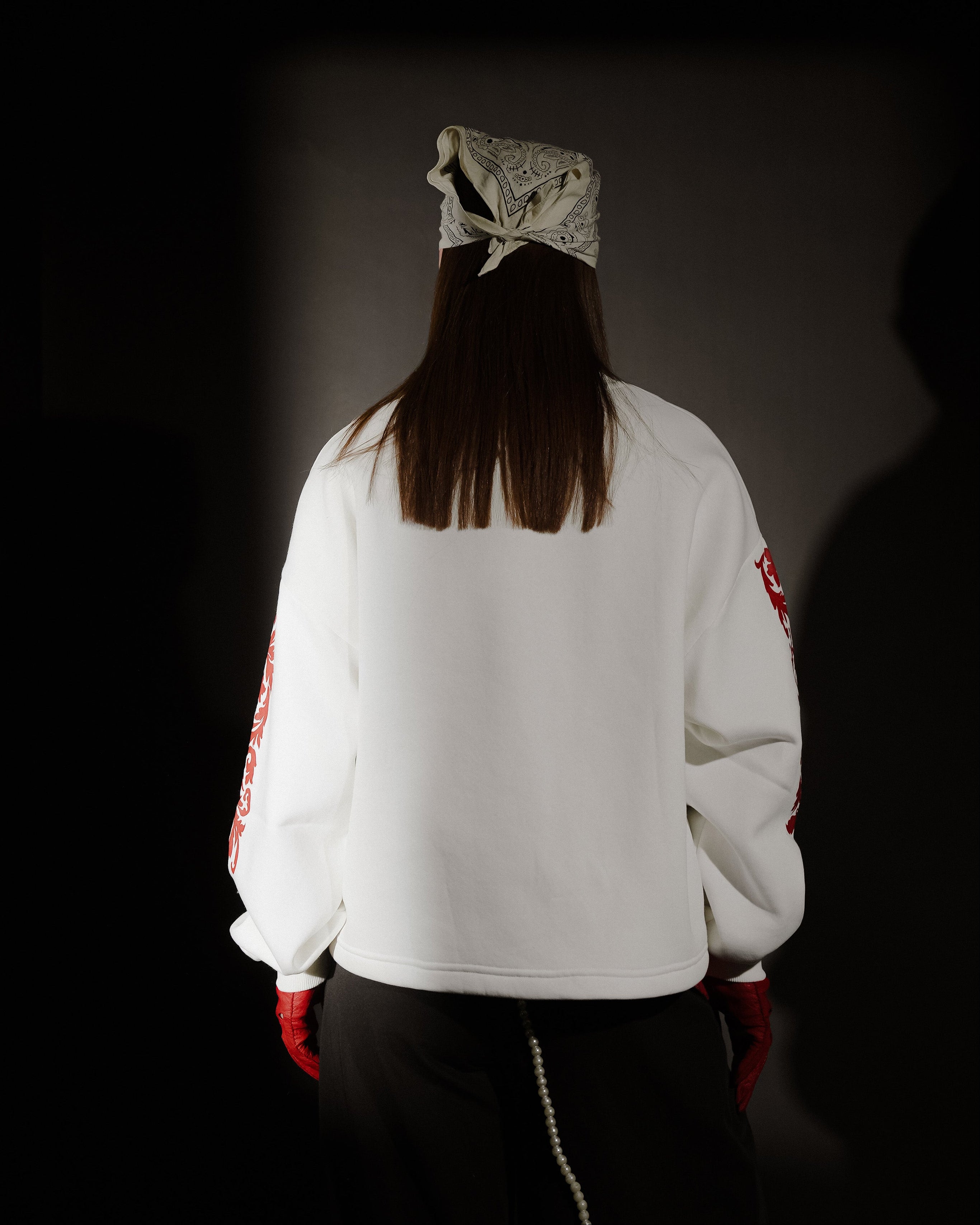 Person wearing a white jacket with red accents and a headscarf, standing against a dark background