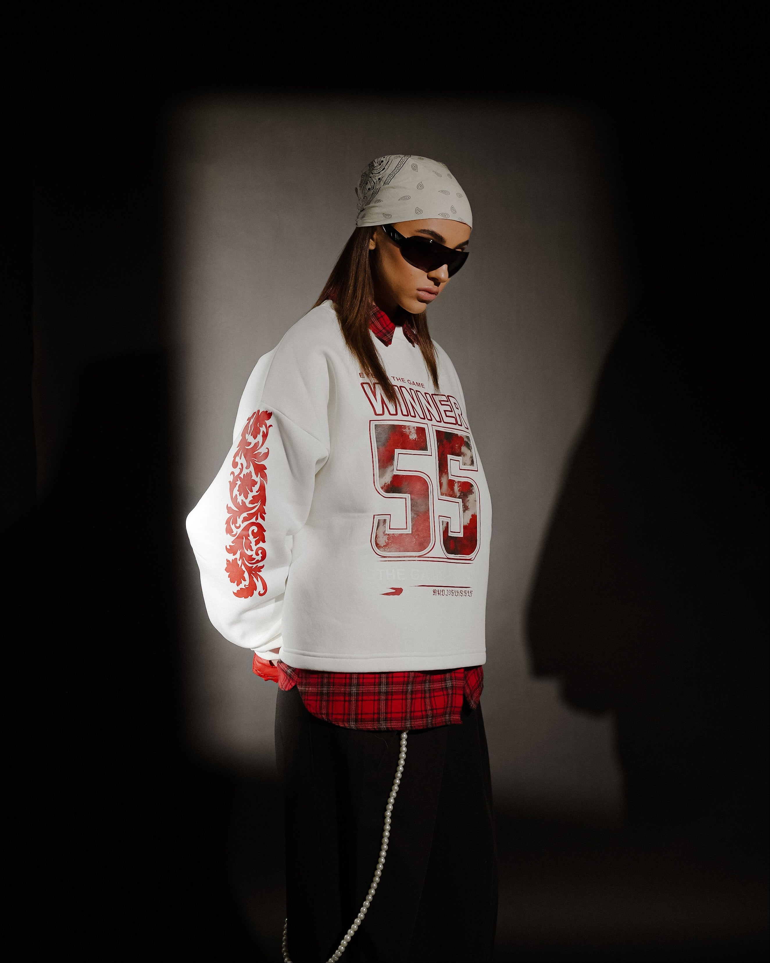 Person wearing a white sweatshirt with red text and numbers, standing against a dark background.