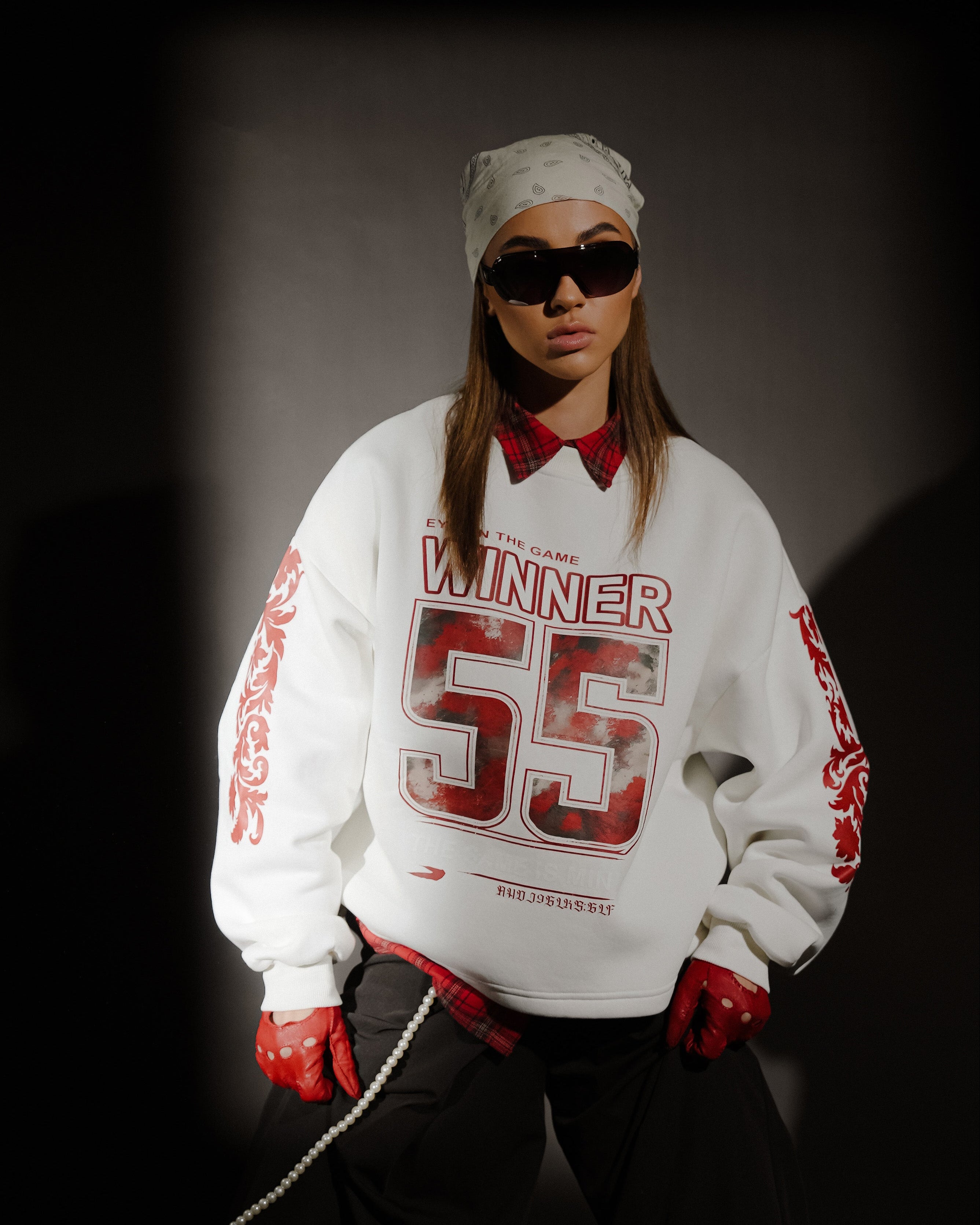 Person wearing a white sweatshirt with red text and graphics, sunglasses, and red gloves on a dark background.