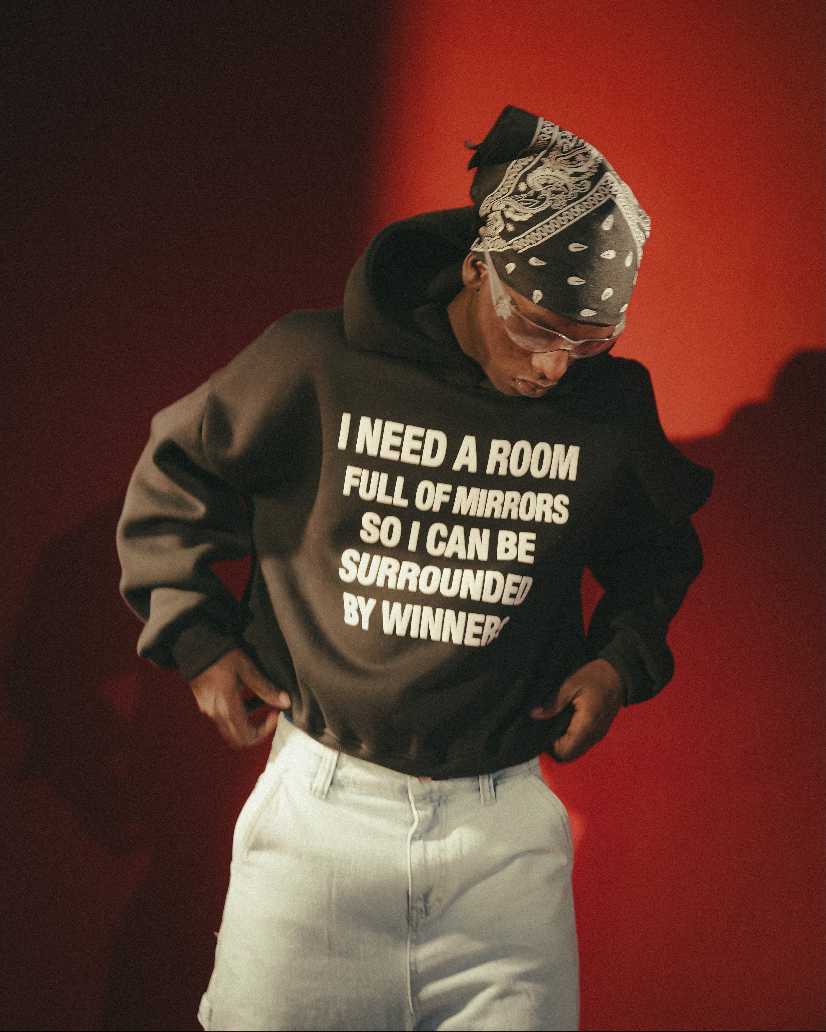 Person wearing a black hoodie with text and white pants against a red background