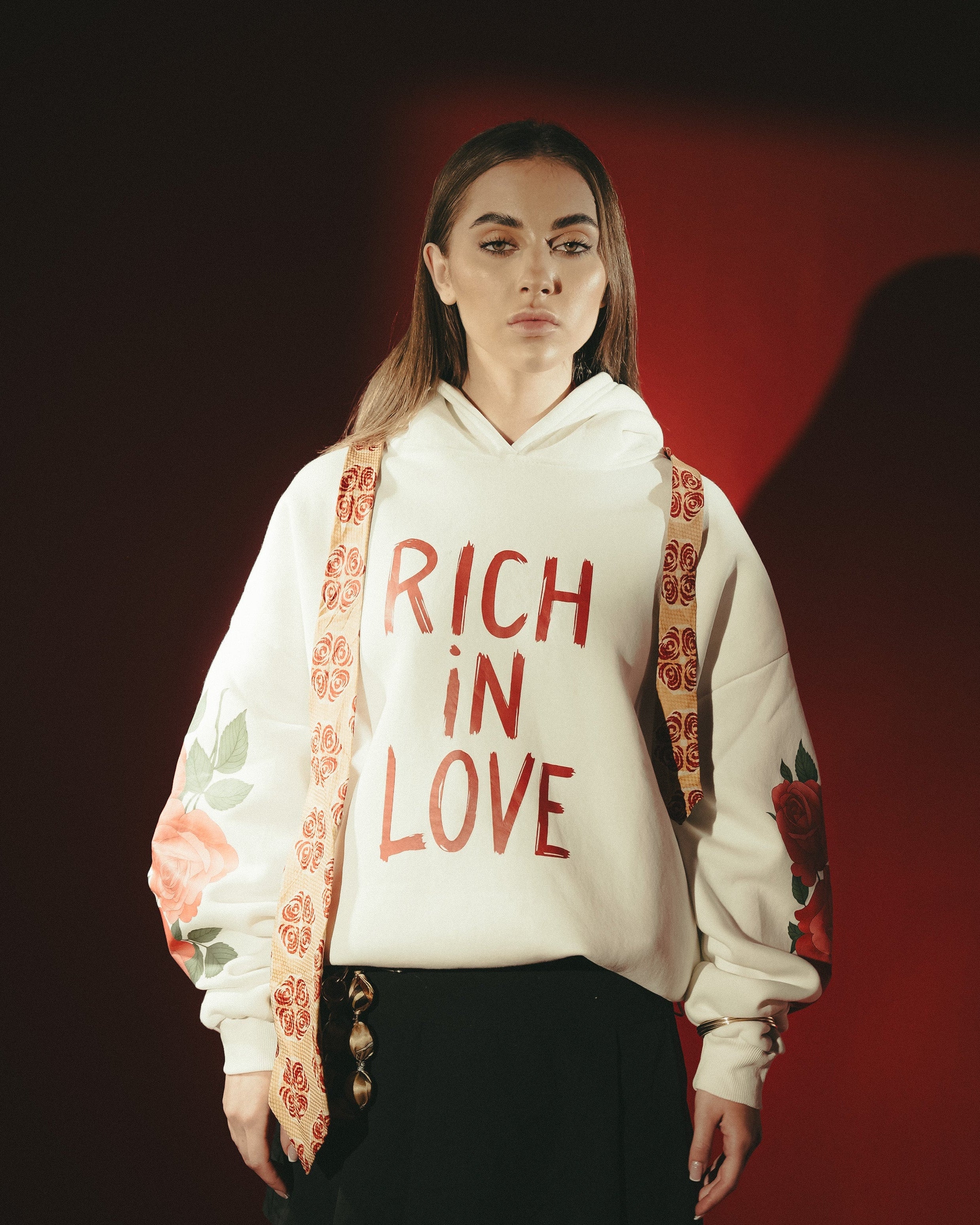 Person wearing a white hoodie with 'Rich in Love' text, floral sleeves, and a red background