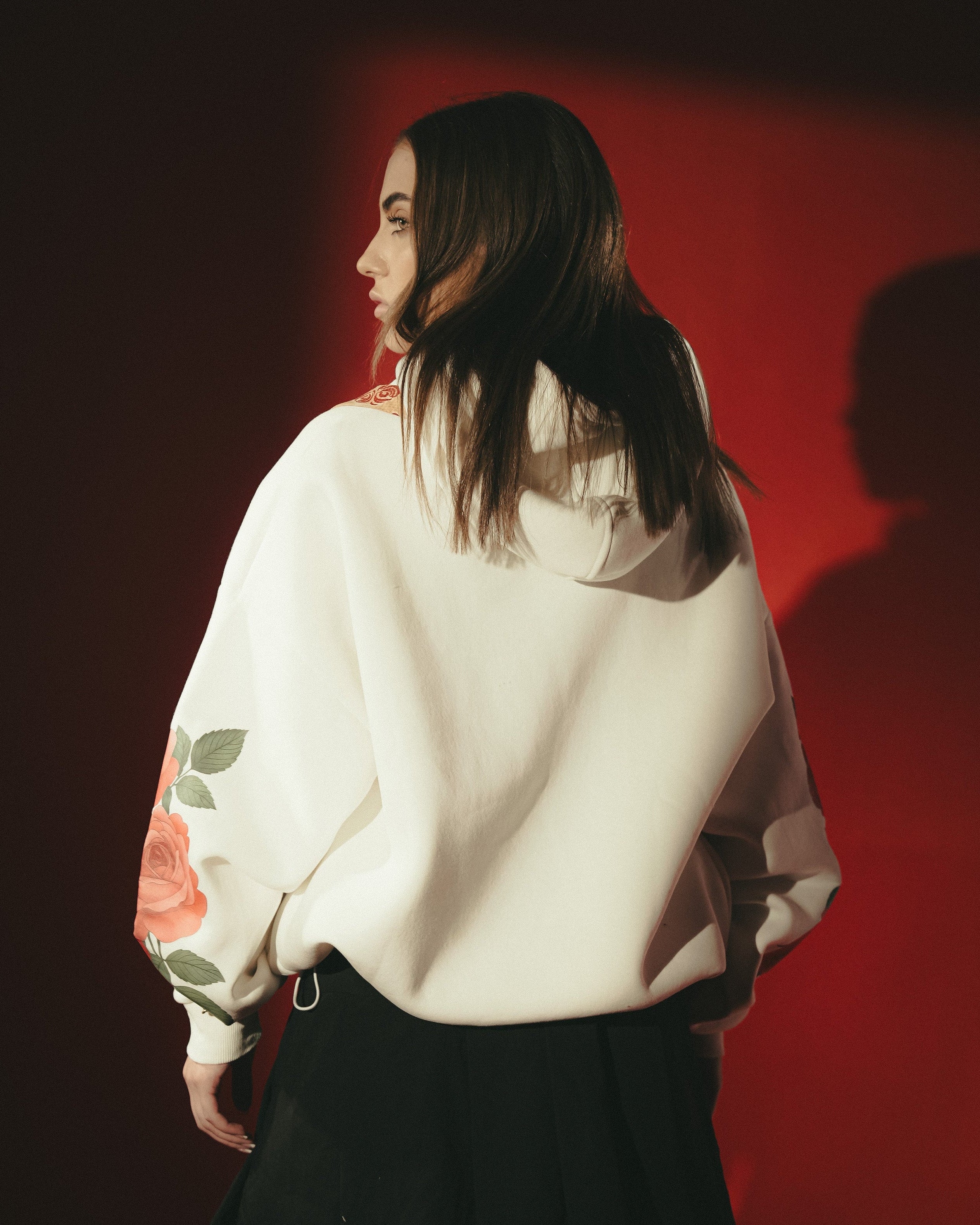 Person wearing a white sweatshirt with floral designs on a red background