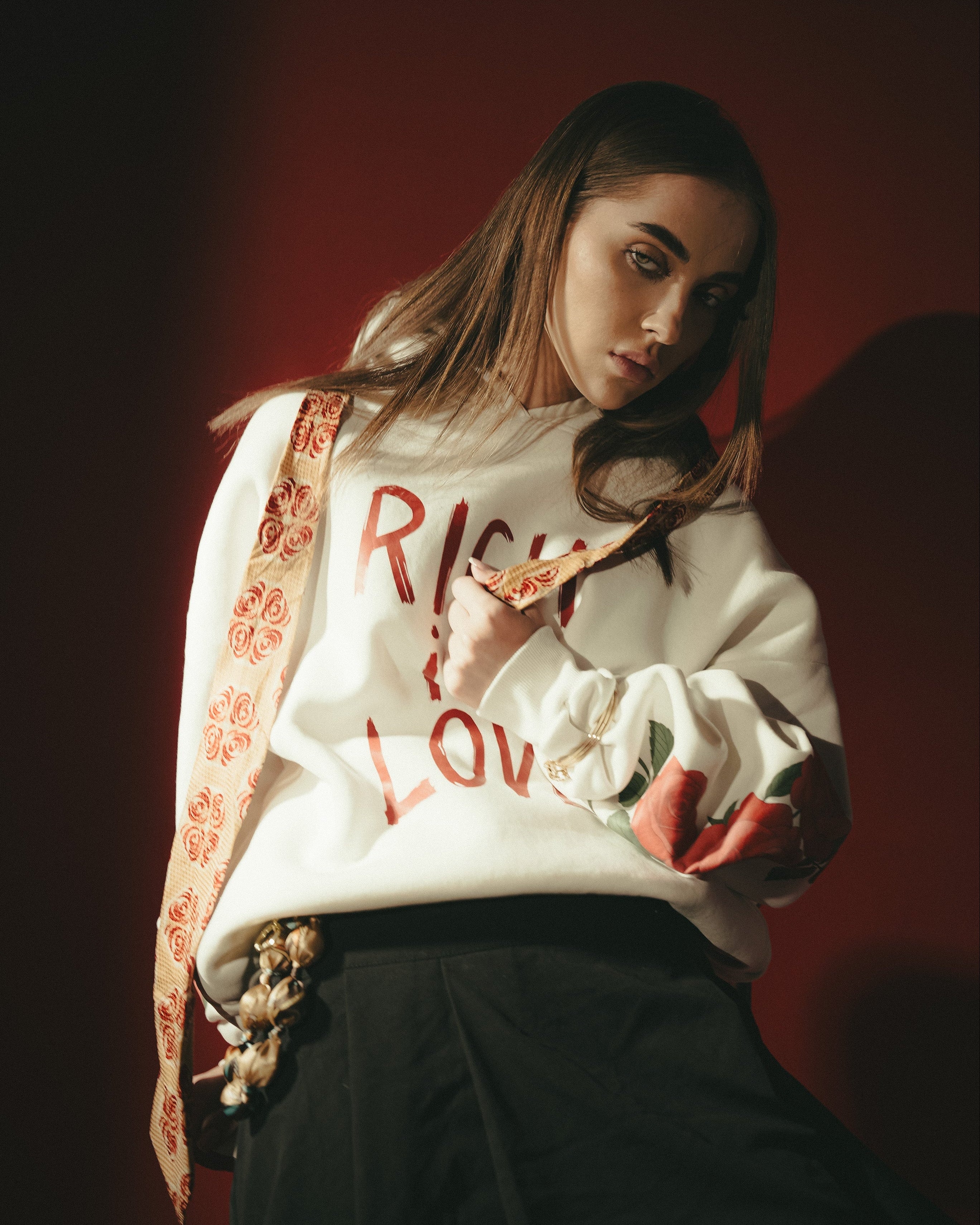 Person wearing a white sweatshirt with text and a floral scarf against a dark background
