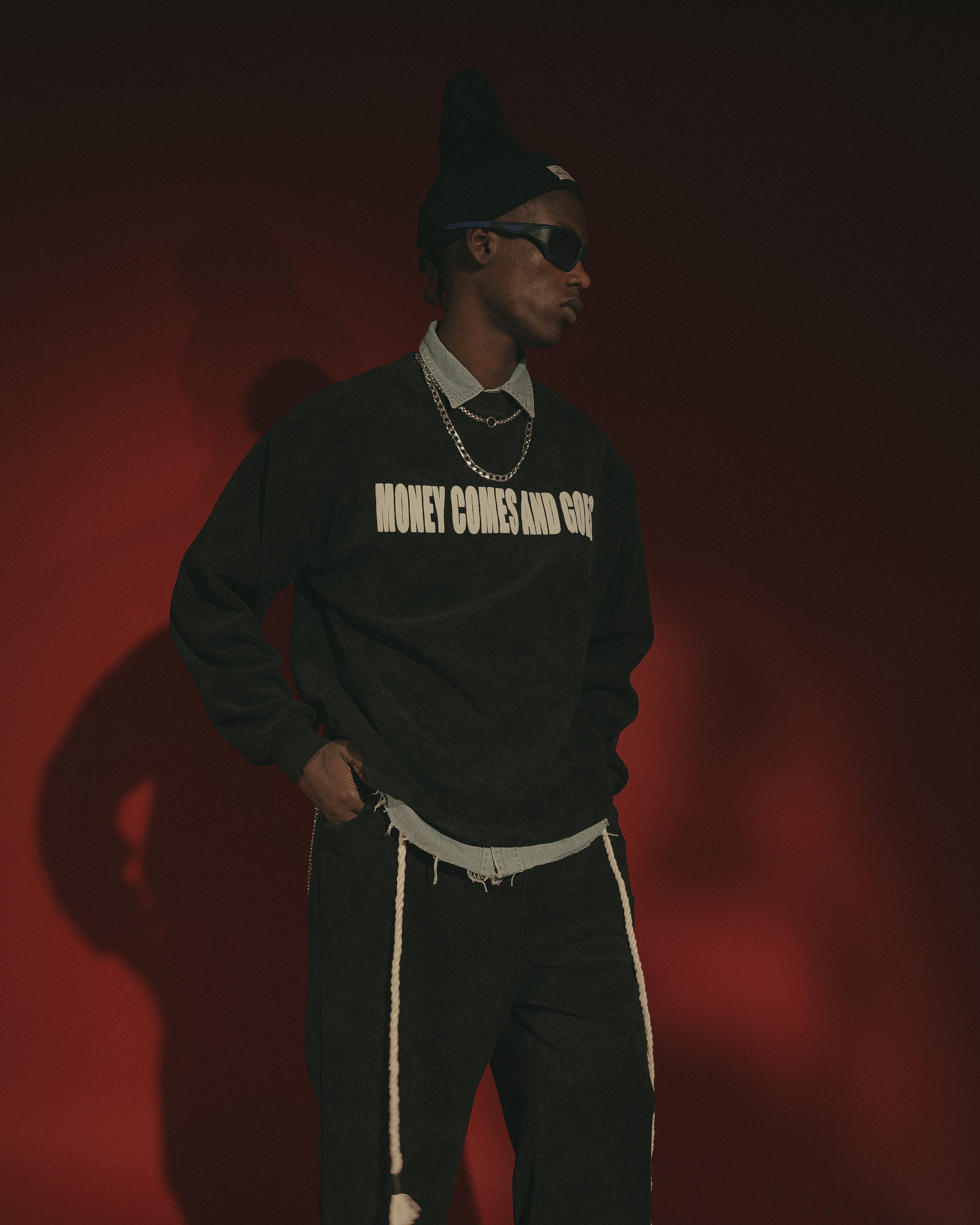 Person wearing a black sweatshirt with text, standing against a red background