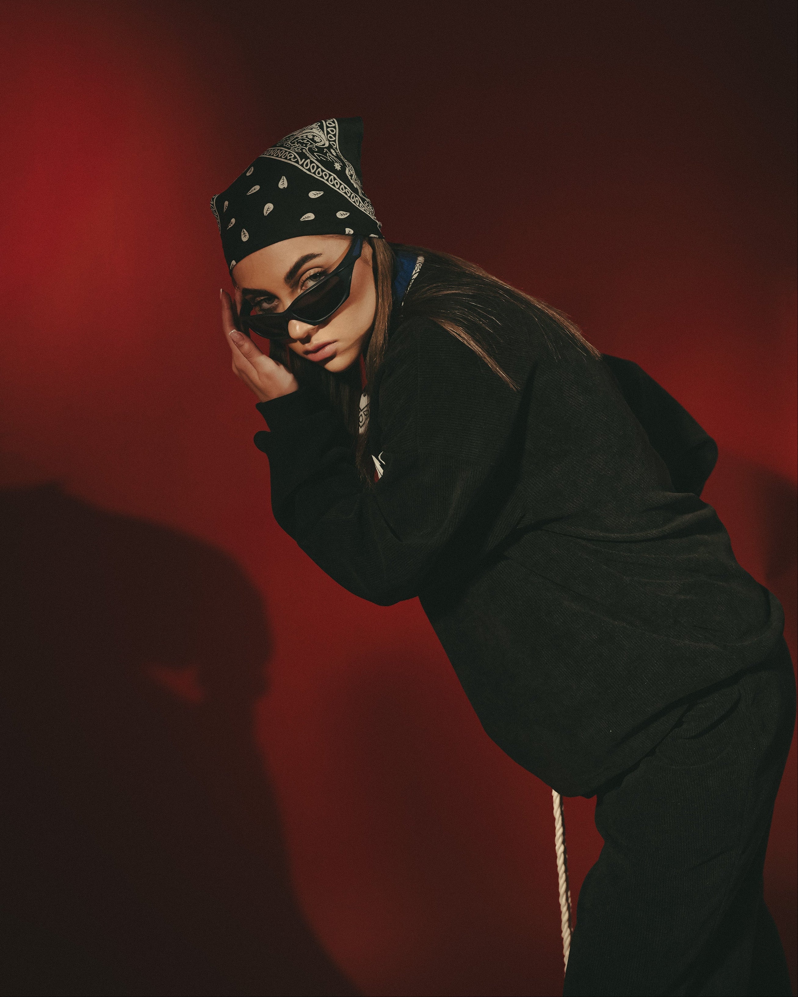 Person wearing a black outfit and headscarf with a red background