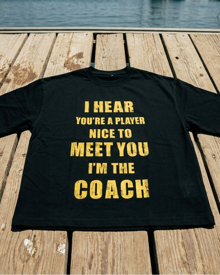 Black t-shirt with yellow text on a wooden dock with boats in the background