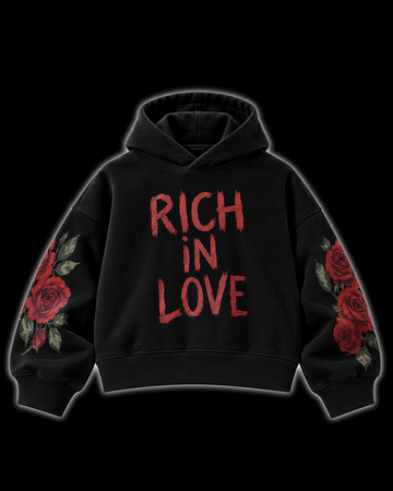 A black pullover hoodie with 'RICH IN LOVE' printed in distressed red letters across the chest, featuring red rose and green leaf illustrations on both sleeves, shown against a solid black background.