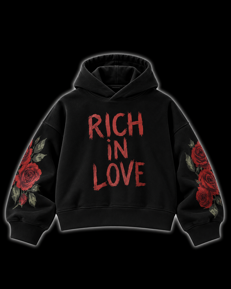 A black pullover hoodie with 'RICH IN LOVE' printed in distressed red letters across the chest, featuring red rose and green leaf illustrations on both sleeves, shown against a solid black background.