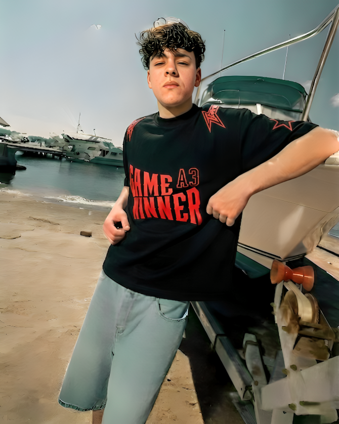 Person wearing a black t-shirt with 'GAME WINNER' text by a waterfront with boats and buildings in the background.