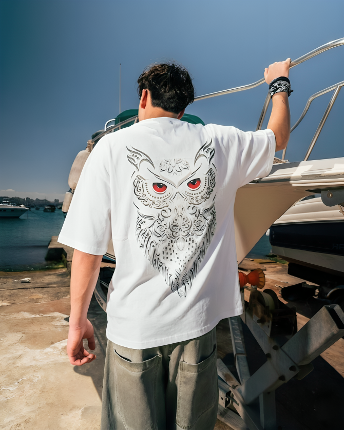 Person wearing a white t-shirt with an owl design on a boat docked at a harbor.