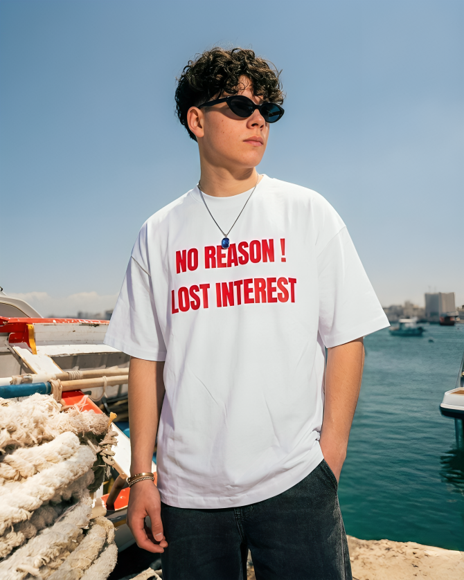 Person wearing a white t-shirt with red text by a waterfront