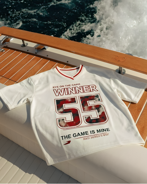 White t-shirt with red and black graphics on a boat deck with water in the background