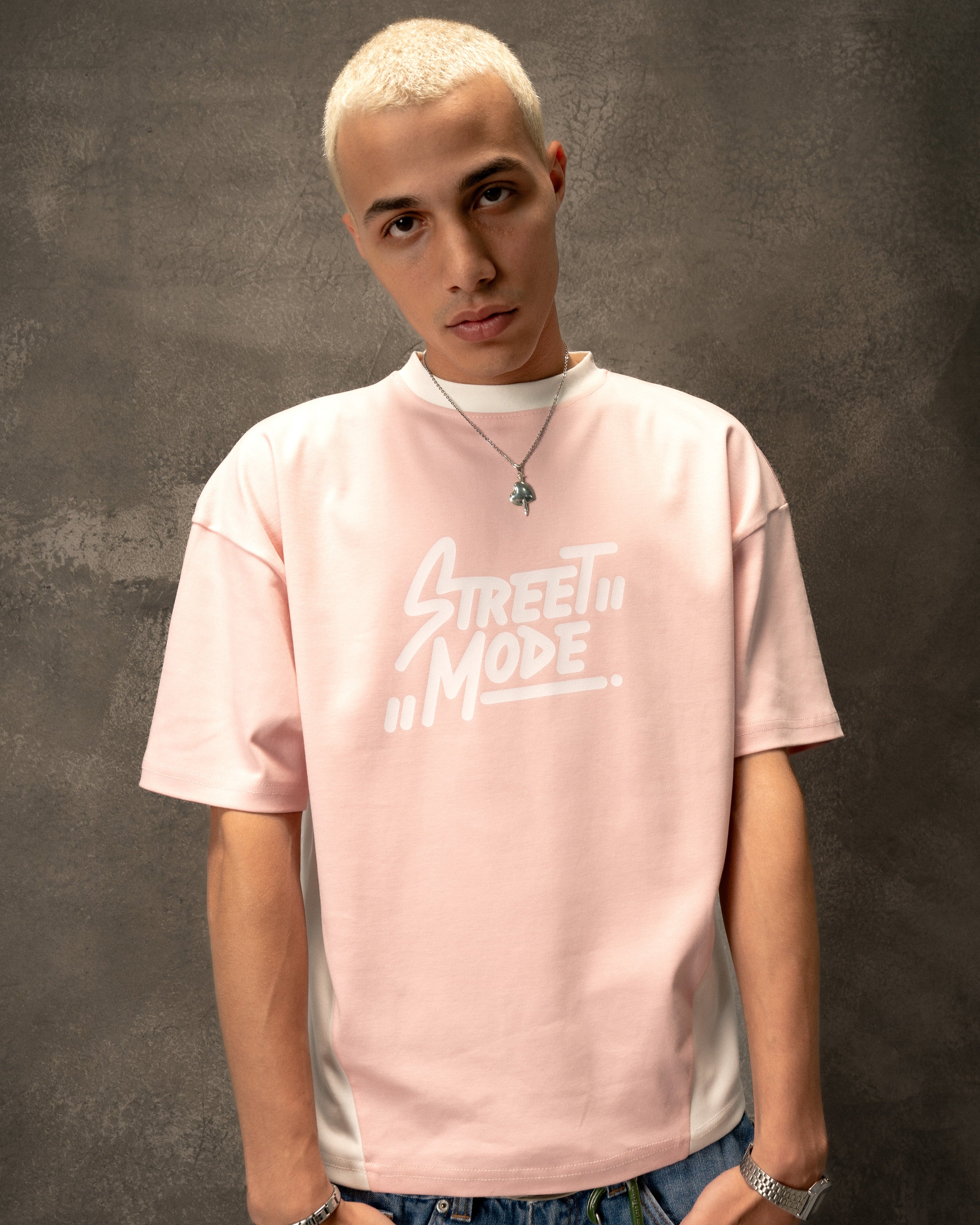 Person wearing a pink t-shirt with text and blue jeans against a dark background