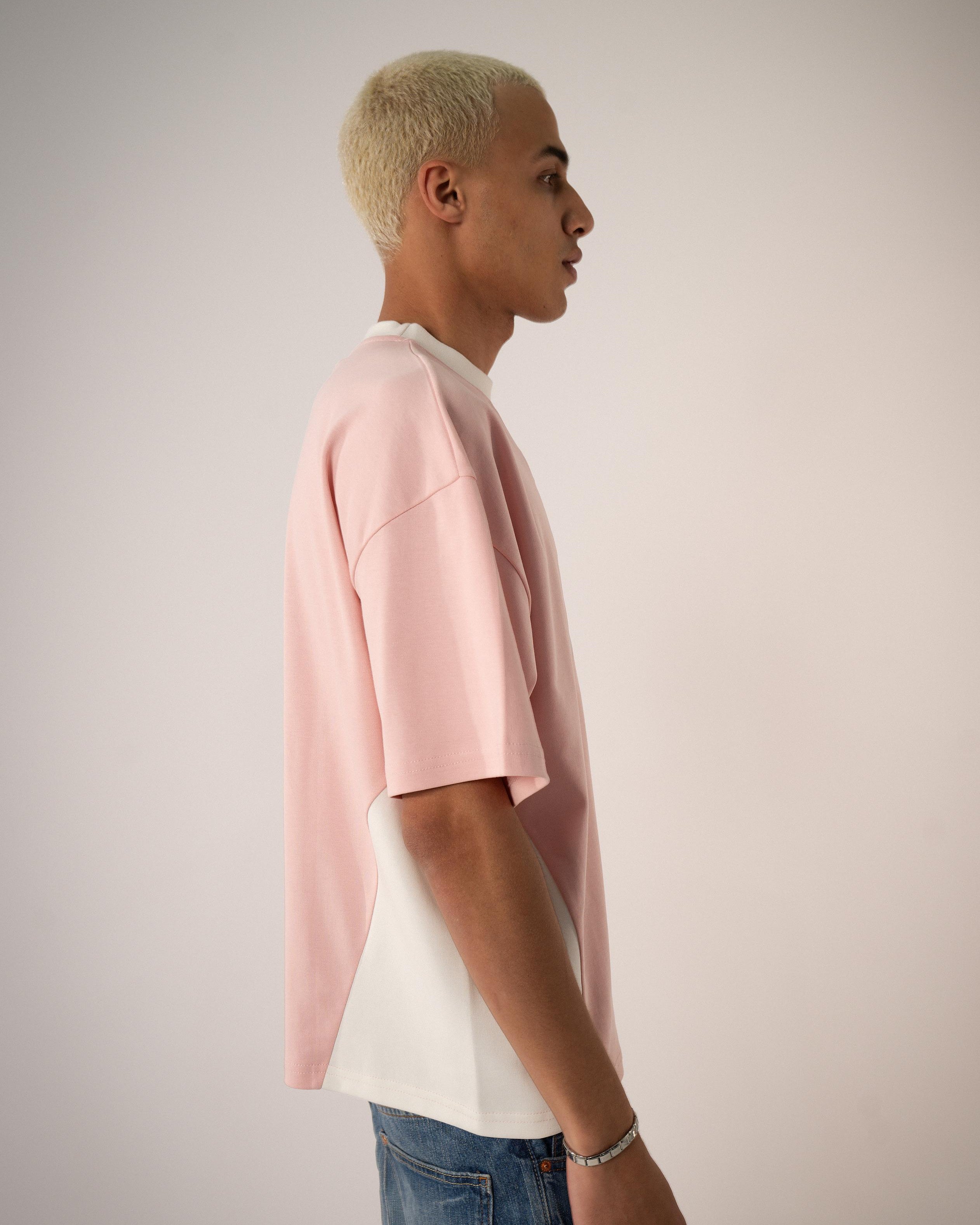 Person wearing a pink t-shirt over a white shirt with blue jeans on a plain background