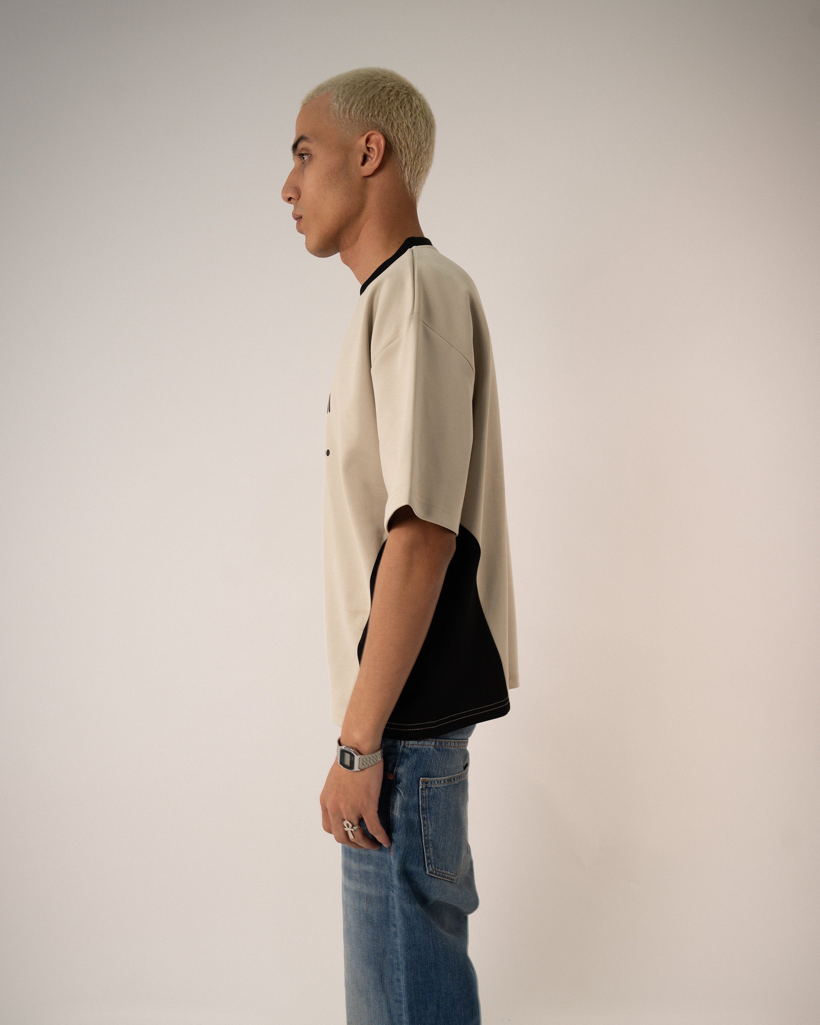 Person wearing a beige jacket over a black shirt with blue jeans on a plain background